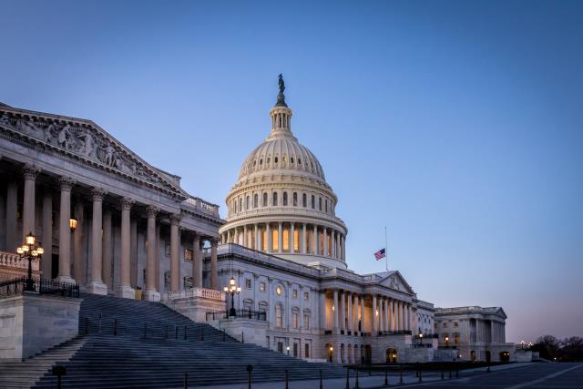 **Alt text:** The U.S. Capitol building in Washington, D.C., illuminated at dusk, with the Capitol dome centered and the House and Senate wings extending on either side under a clear evening sky.